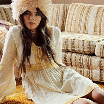 Hero banner for The Hippie Shake's embroidered and bohemian dresses - Model sits on floor wearing white dress.