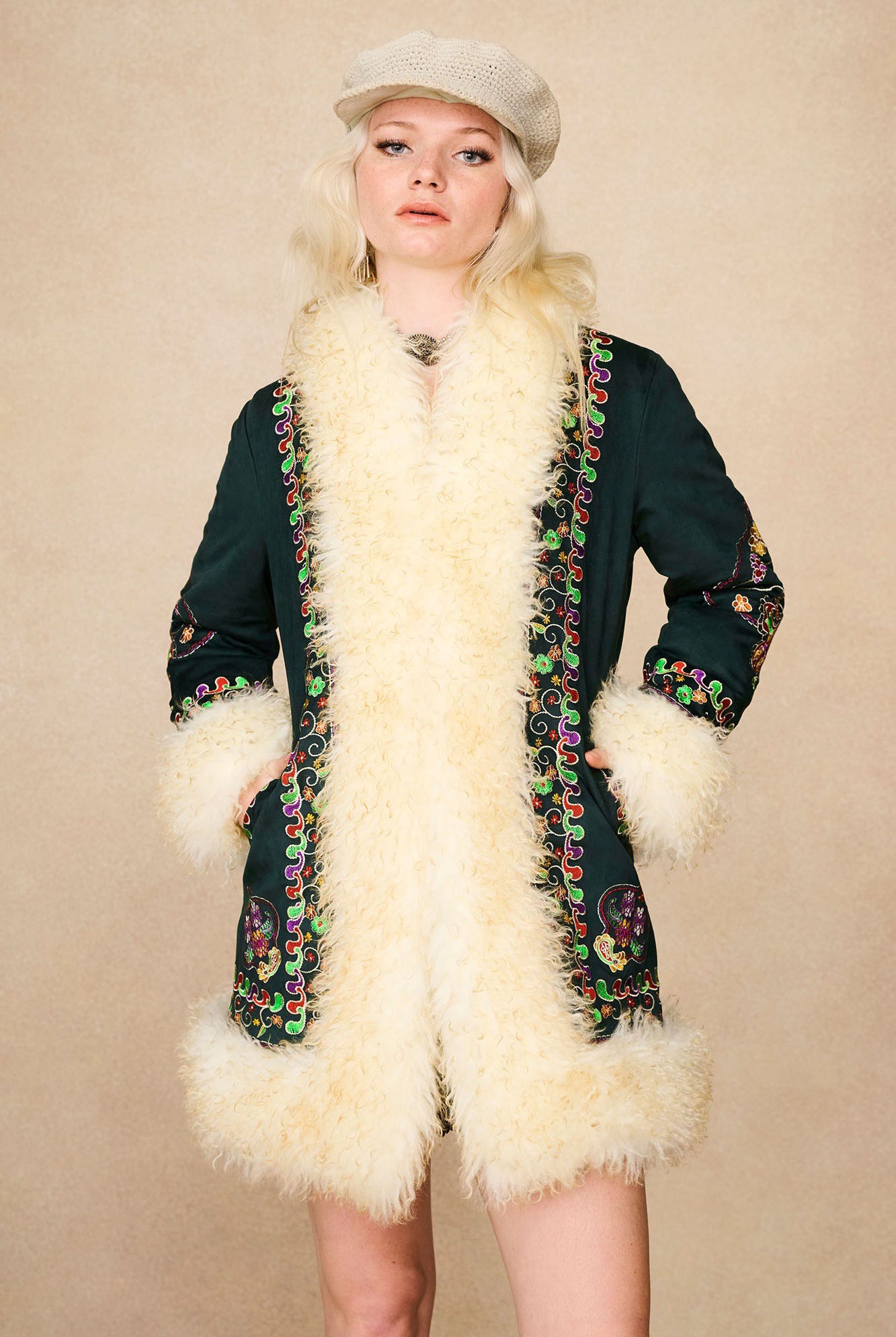 Model wearing The Hippie Shake's green embroidered Penny Lane coat with hands in pockets and neutral expression.