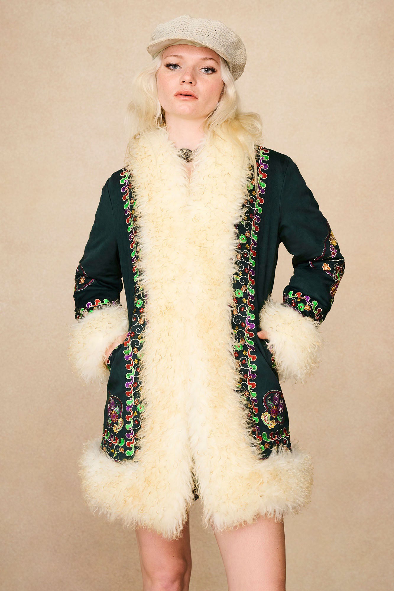 Model wearing The Hippie Shake's green embroidered Penny Lane coat with hands in pockets and neutral expression.