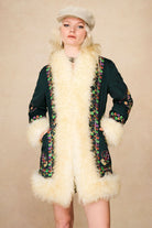 Model wearing The Hippie Shake's green embroidered Penny Lane coat with hands in pockets and neutral expression.
