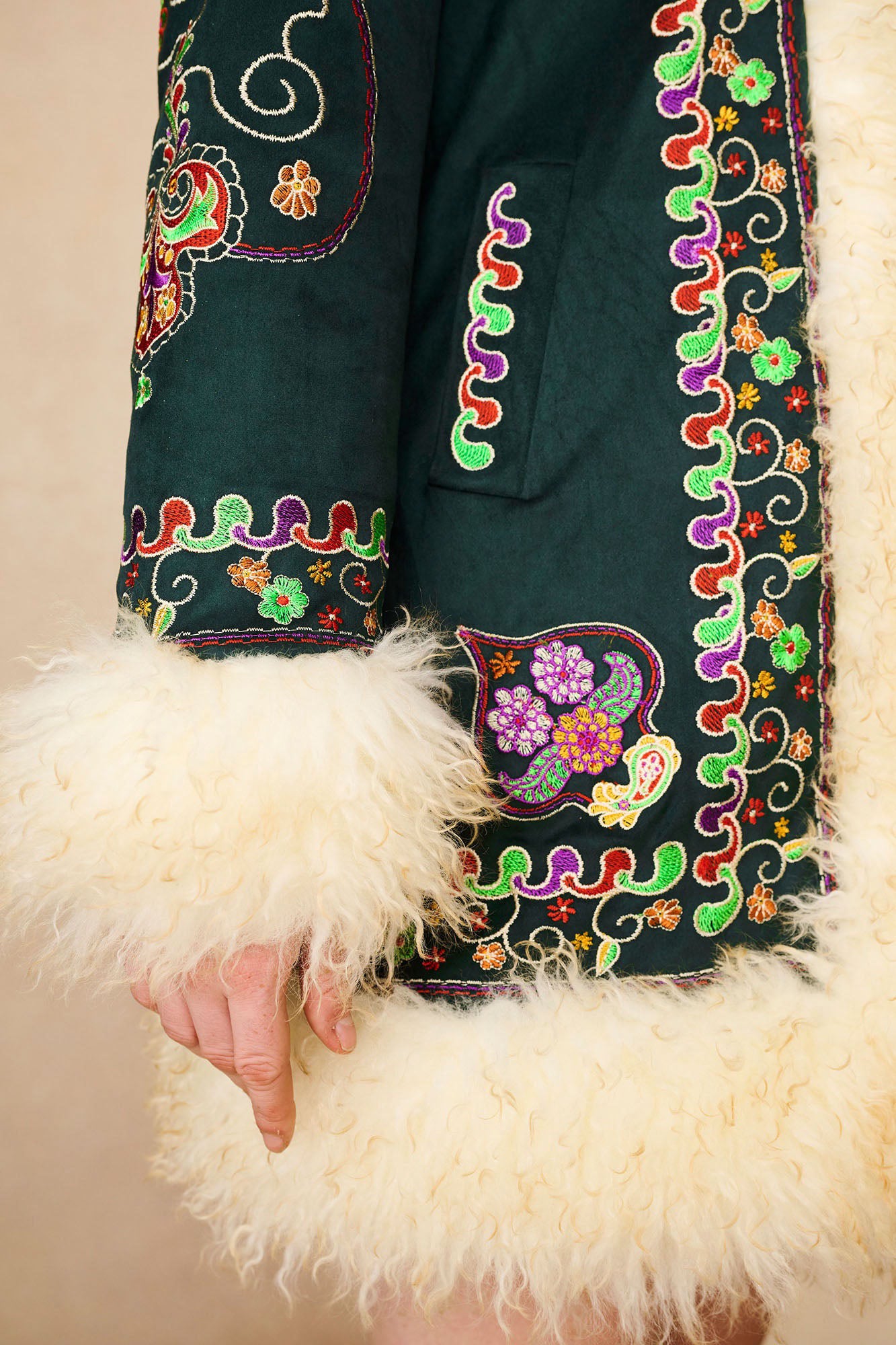 Close-up of The Hippie Shake's green afghan coat showing multicoloured floral stitching and shearling trim.