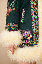 Close-up of The Hippie Shake's green afghan coat showing multicoloured floral stitching and shearling trim.