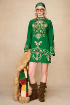 Model holding The Hippie Shake's patchwork Penny Lane coat styled with a green embroidered mini dress.