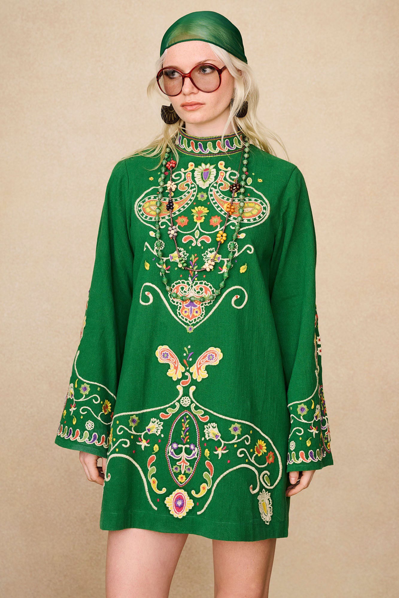 Model styling The Hippie Shake's green embroidered mini dress with statement earrings and layered beaded necklaces.