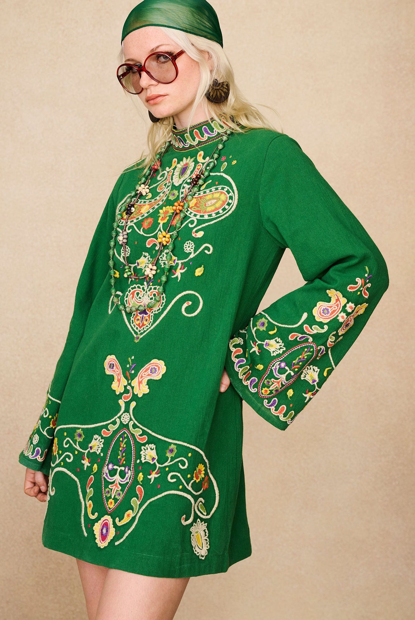 Side view of model in The Hippie Shake's green embroidered mini dress showing wide sleeves and paisley embroidery.