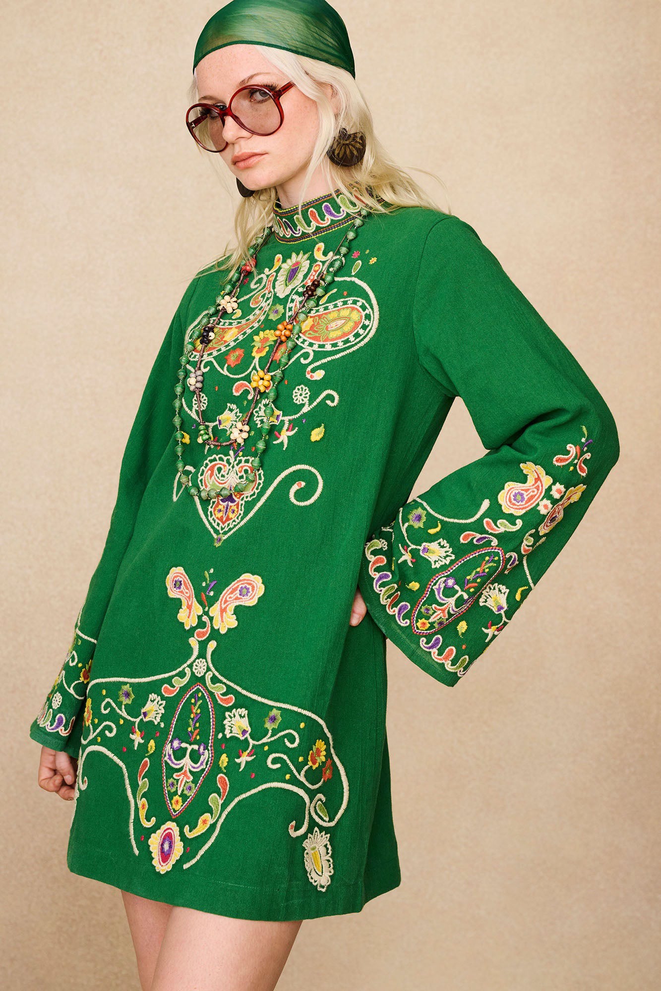 Side view of model in The Hippie Shake's green embroidered mini dress showing wide sleeves and paisley embroidery.