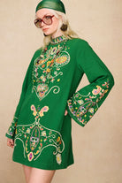 Side view of model in The Hippie Shake's green embroidered mini dress showing wide sleeves and paisley embroidery.