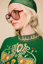 Close-up of The Hippie Shake's green embroidered mini dress showing the high neckline and colourful embroidery details.