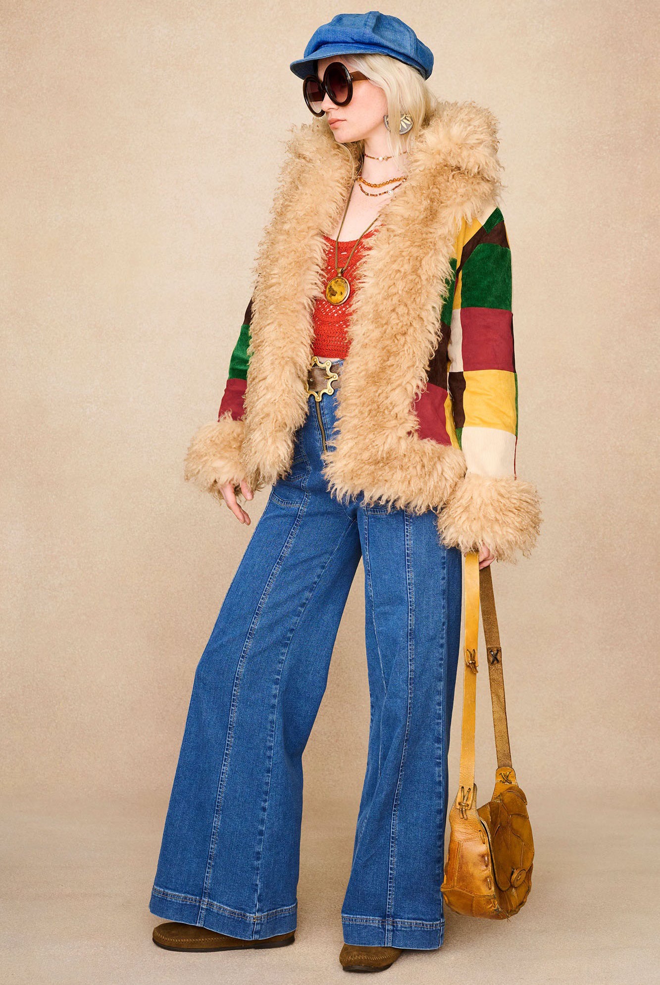 Model wearing The Hippie Shake's chevron flared denim jeans with patchwork coat, red crochet top and tan bag.