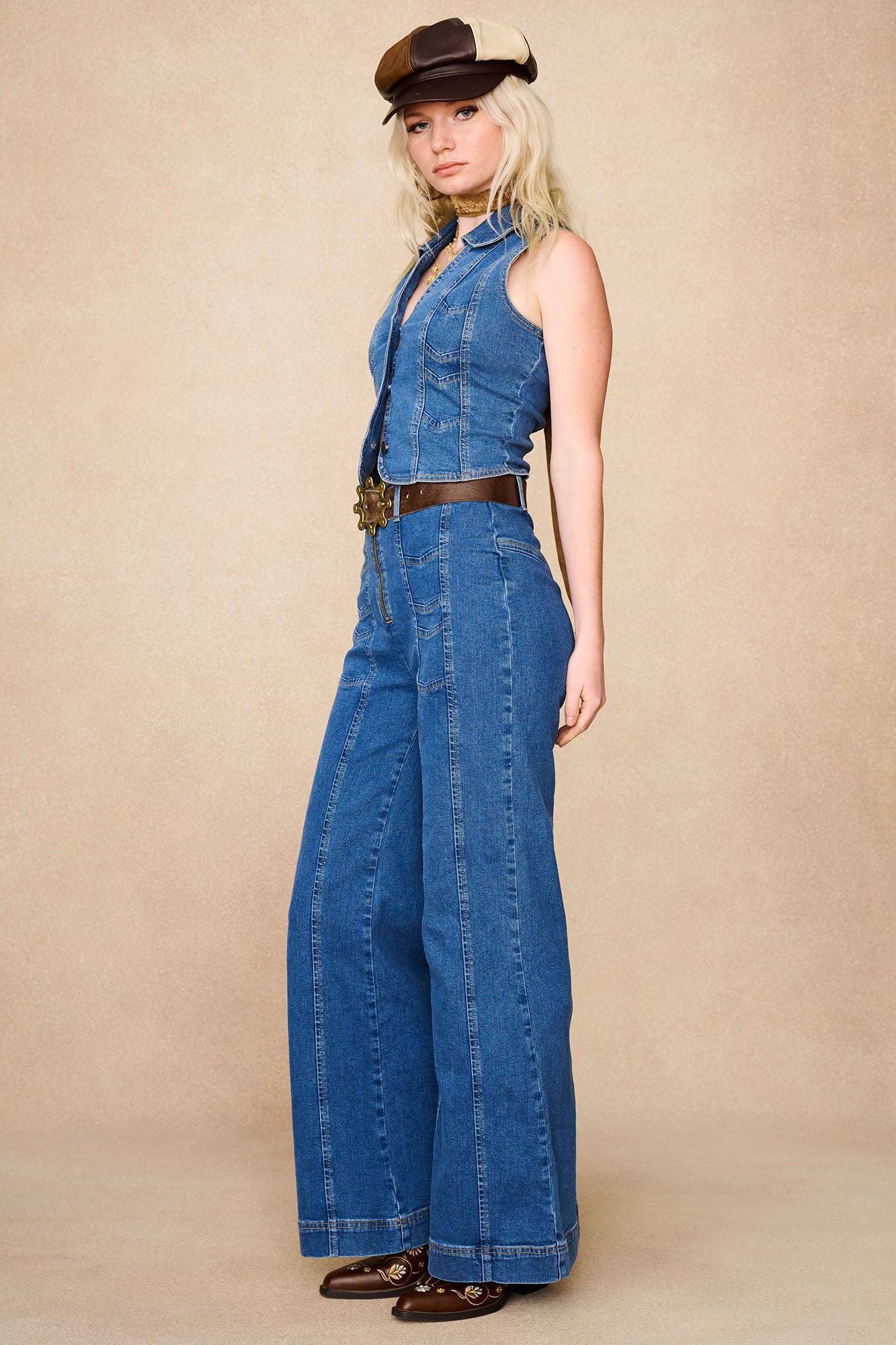 Side profile of The Hippie Shake's chevron flared denim jeans styled with matching vest and panelled baker hat.