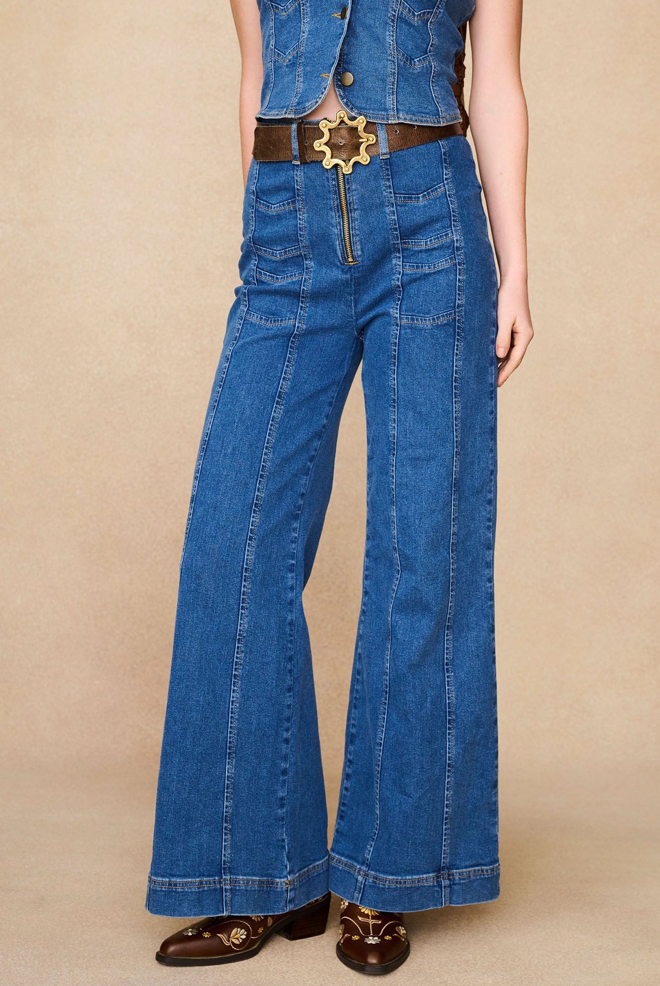 Close-up of The Hippie Shake's 70s style chevron flared denim jeans with exposed zip, brown belt and embroidered boots.