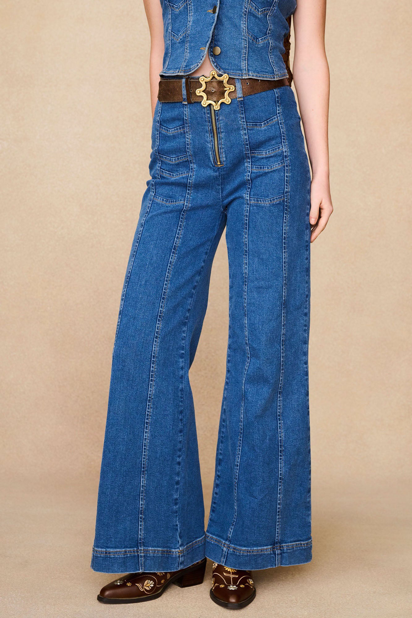 Close-up of The Hippie Shake's 70s style chevron flared denim jeans with exposed zip, brown belt and embroidered boots.
