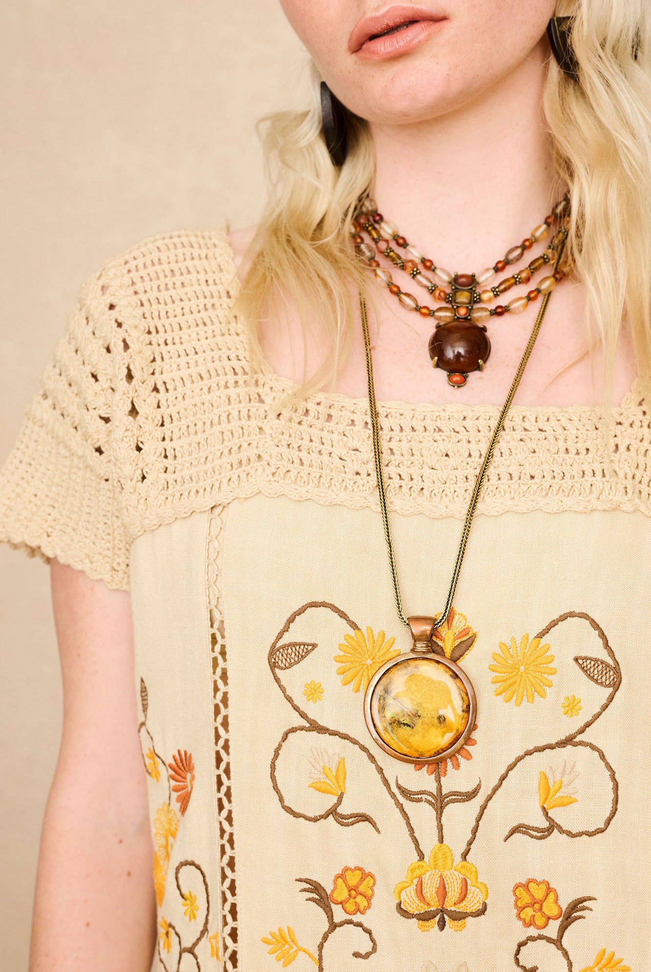 Model wearing The Hippie Shake's cream crochet embroidered midi dress, featuring intricate embroidery in warm retro hues.