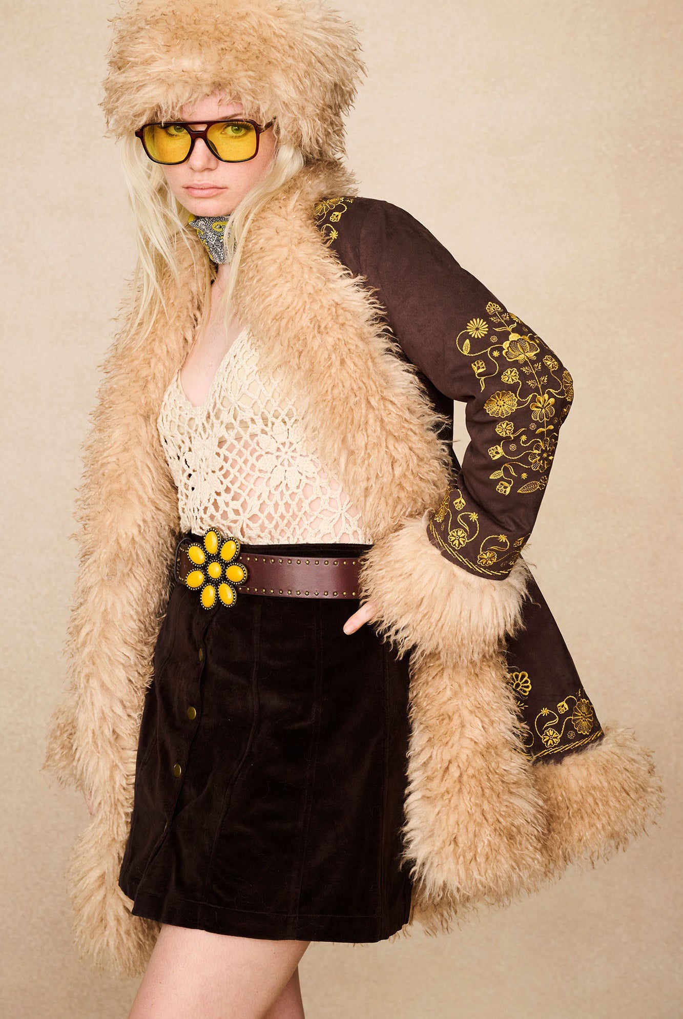 Model in The Hippie Shake's brown velvet mini skirt and faux fur coat, hands on hips.