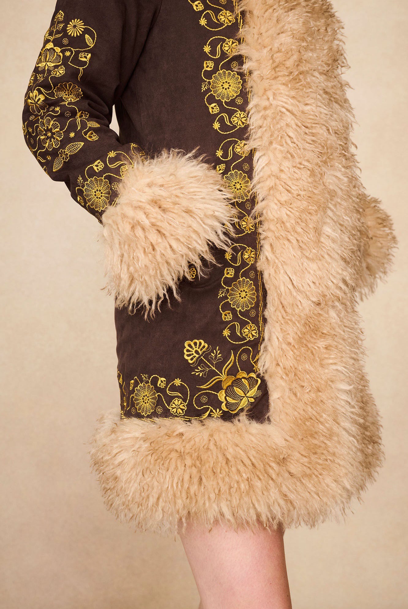 Close-up of The Hippie Shake's 70s inspired brown afghan coat showing golden floral embroidery and faux fur on the sleeve and hem.