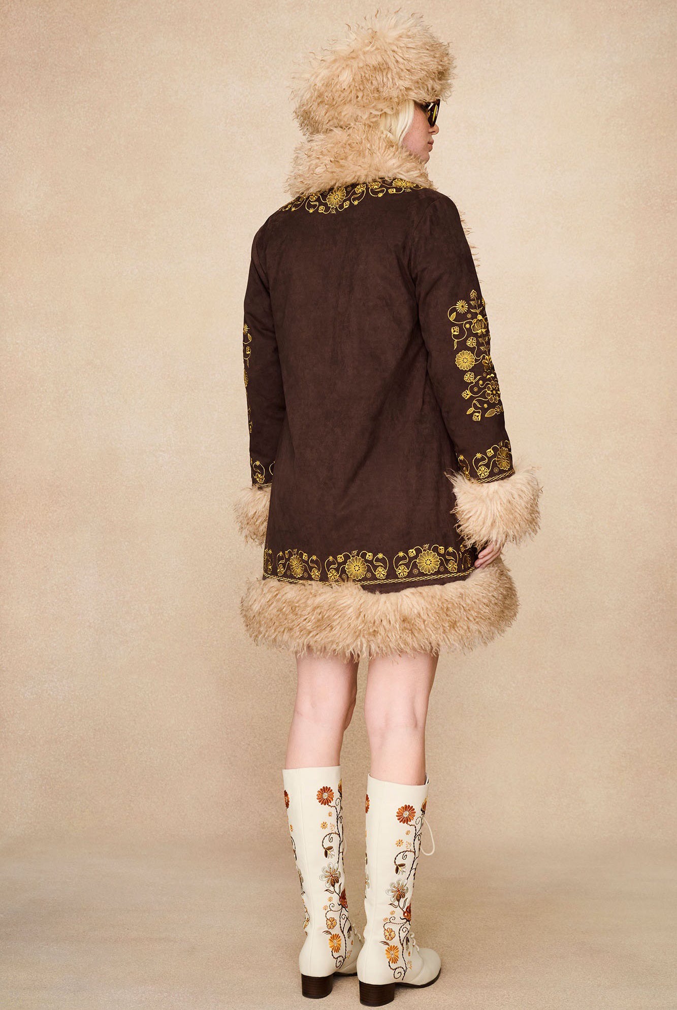 Model wearing The Hippie Shake's brown afghan coat, seen from behind, showing floral embroidery and faux fur hem.