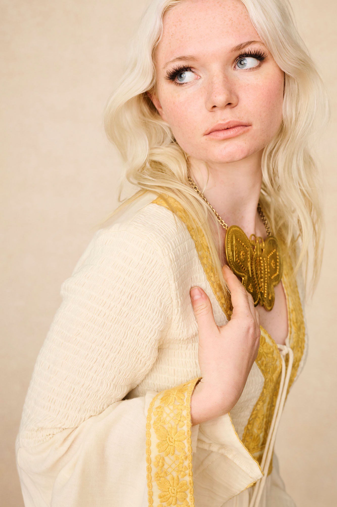 Model close-up of The Hippie Shake's cream lace trim mini dress showing embroidered trims and butterfly necklace.
