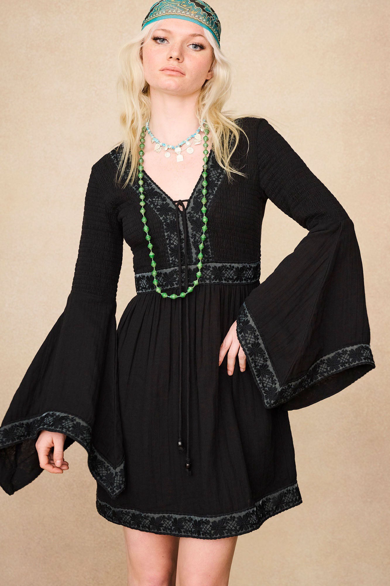 The Hippie Shake's black vintage mini dress with lace trim and flowy sleeves, accentuated with a green bead necklace.