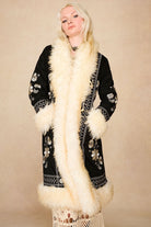 Model wearing the Hippie Shake's black afghan coat with hands in pockets, accentuating the off-white shaggy faux fur trims.