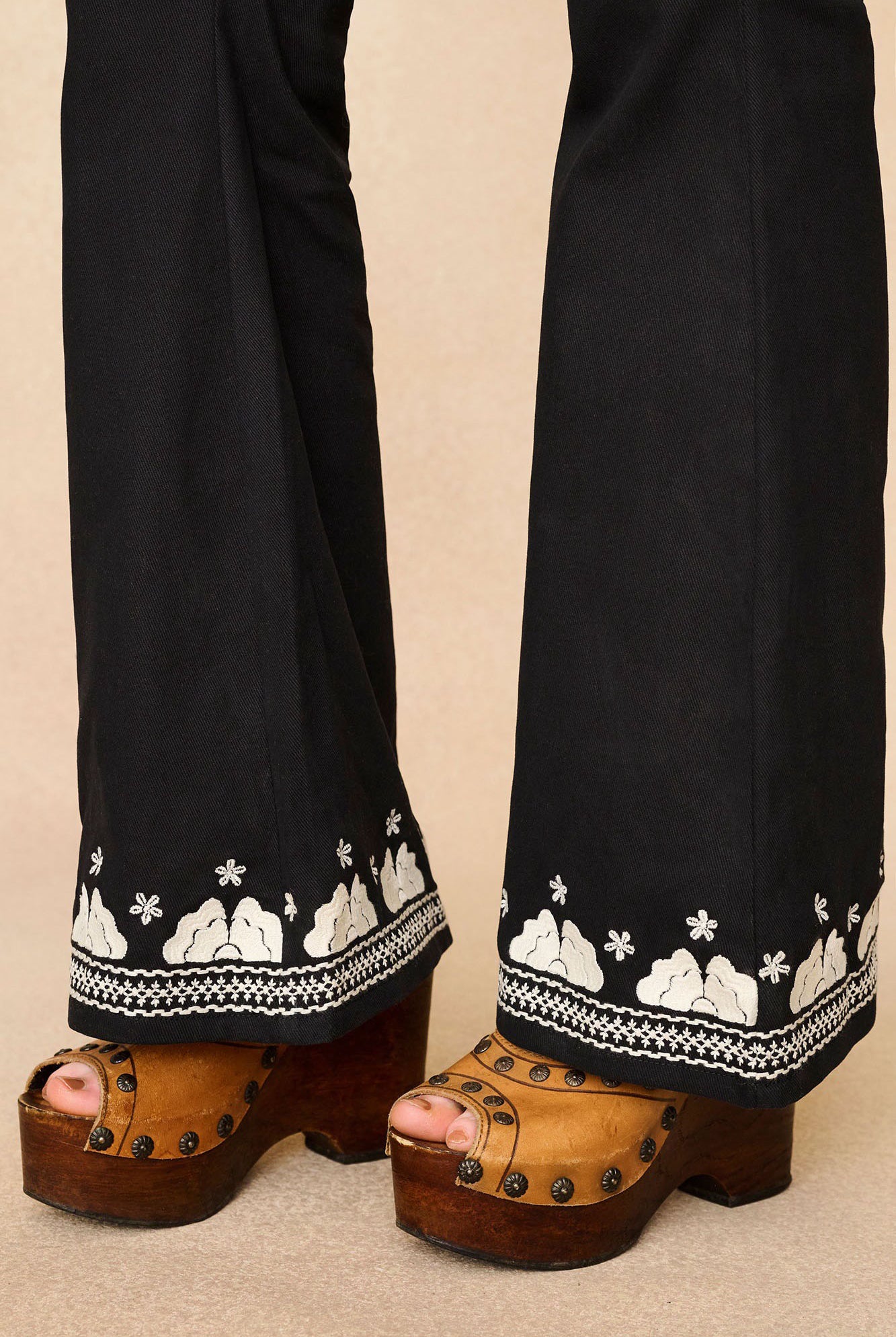 Close-up of The Hippie Shake's 70s style black floral flared trousers featuring the intricate embroidery at the bottom.