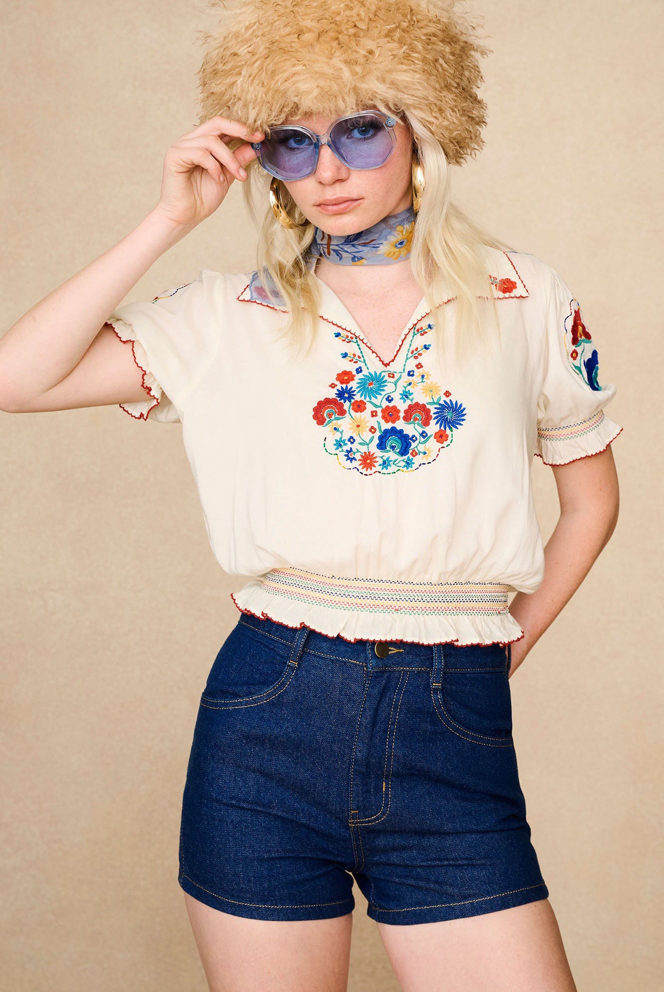 Model wearing The Hippie Shake's vintage high waisted shorts styled with a cream embroidered blouse and blue sunglasses.
