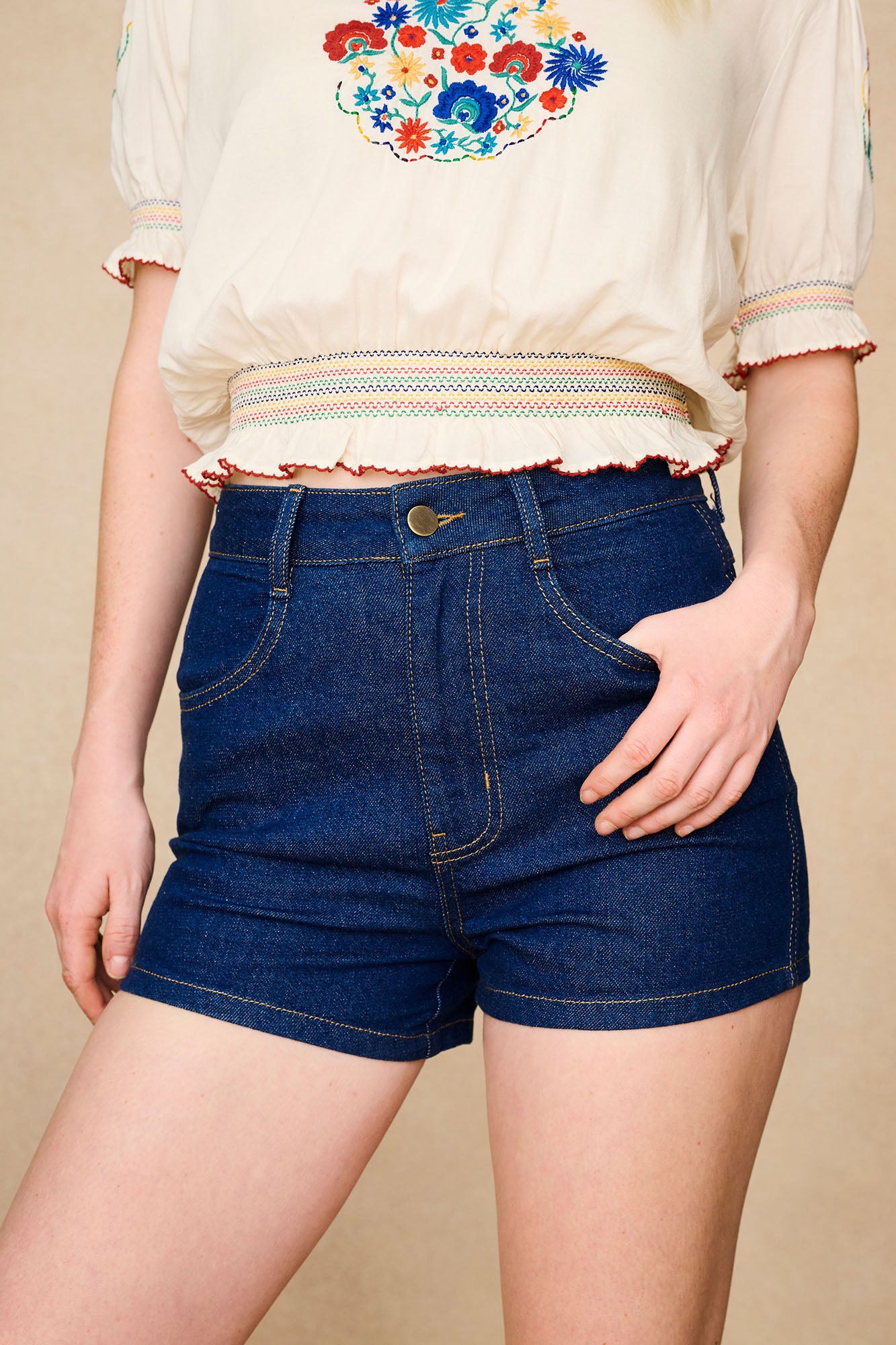 The Hippie Shake's women's high waisted denim shorts paired with a 70s style embroidered cream top.