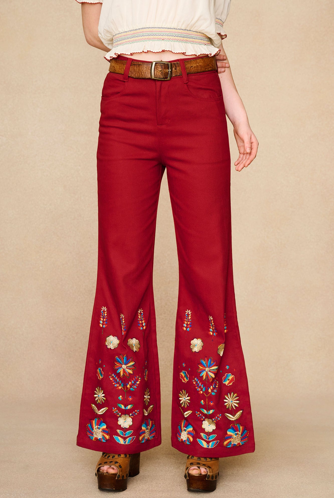 The Hippie Shake's red embroidered flared trousers with intricate floral designs in blue, gold, and orange at the hem.