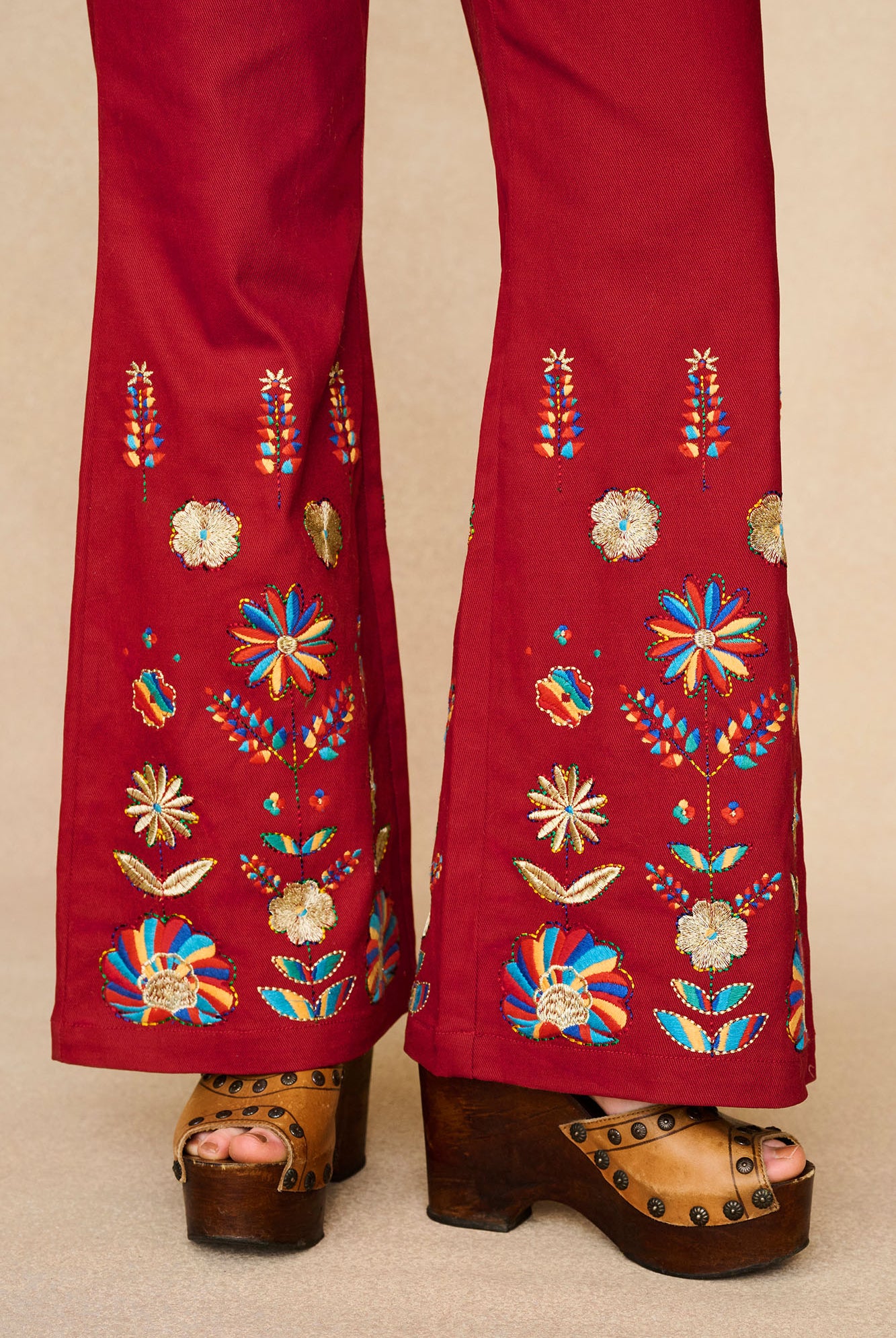Close-up of The Hippie Shake's red embroidered flared trousers showing detailed gold and multicolour floral embroidery.