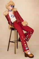 Model lounging in The Hippie Shake's red embroidered Penny Lane coat paired with high-waisted flares and vintage sunglasses.
