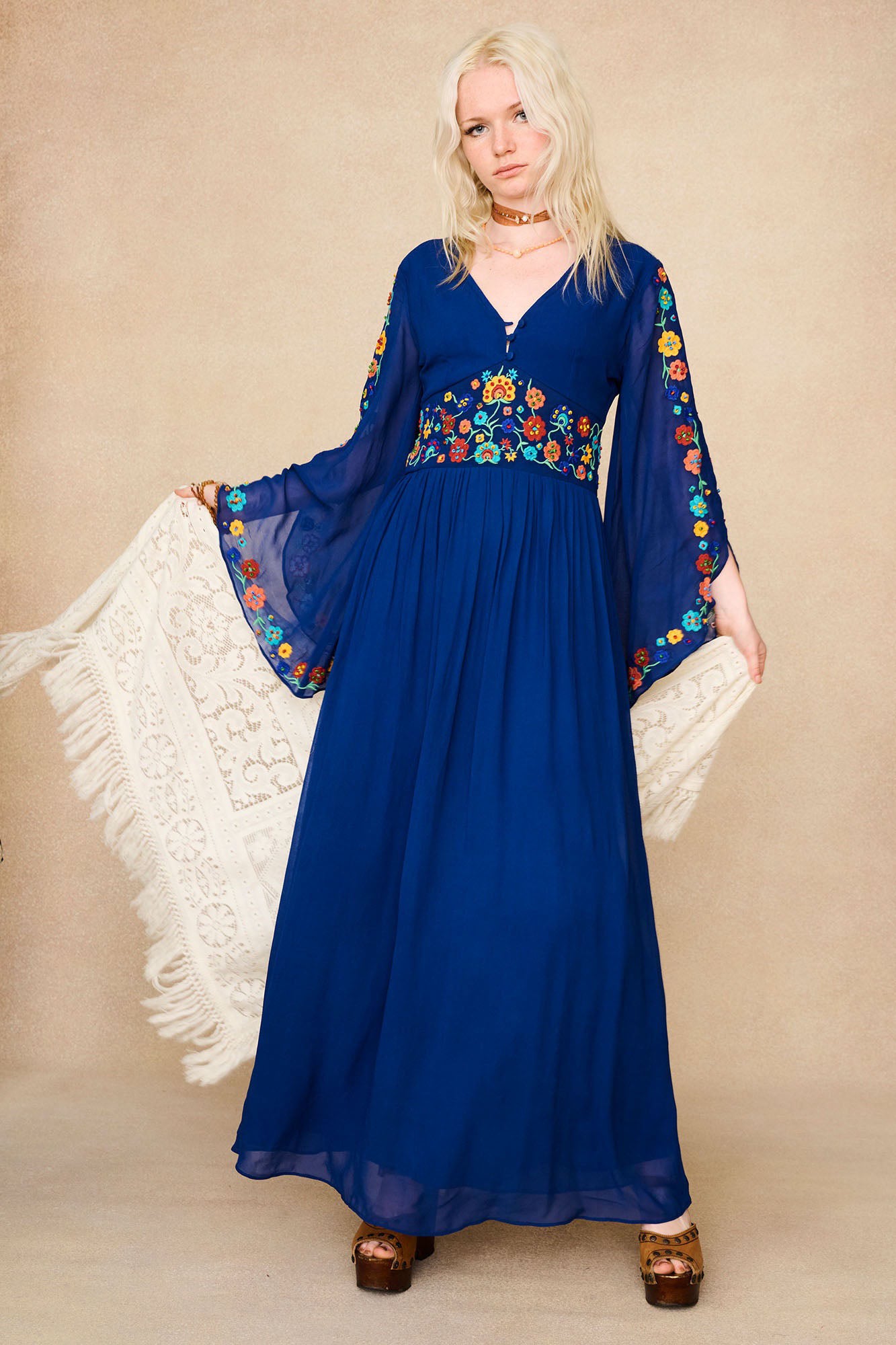 Full-length shot of model in The Hippie Shake's blue vintage embroidered maxi dress holding a white crochet shawl.