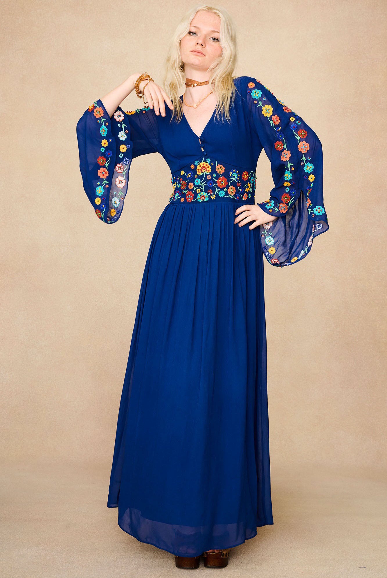 Model wearing The Hippie Shake's blue vintage embroidered maxi dress with flared sleeves and floral detailing on bodice and arms.