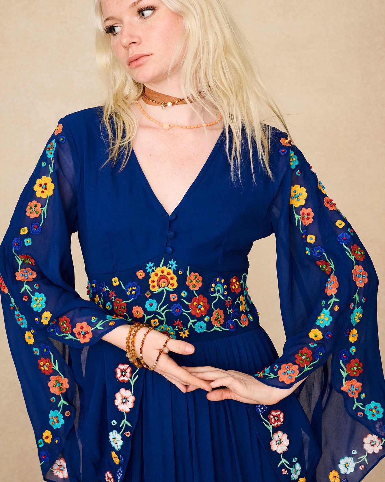 Close-up of The Hippie Shake's blue floral embroidered maxi dress showing colourful floral details on sheer sleeves and waistband.