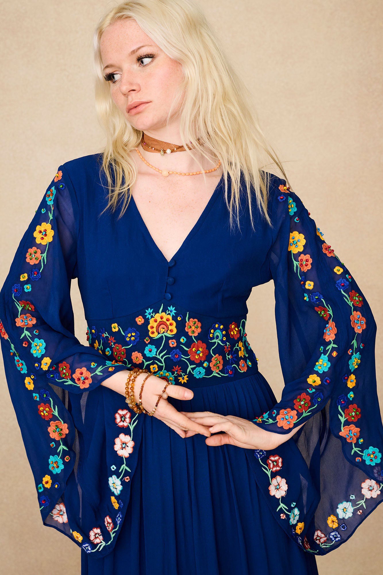 Close-up of The Hippie Shake's blue floral embroidered maxi dress showing colourful floral details on sheer sleeves and waistband.