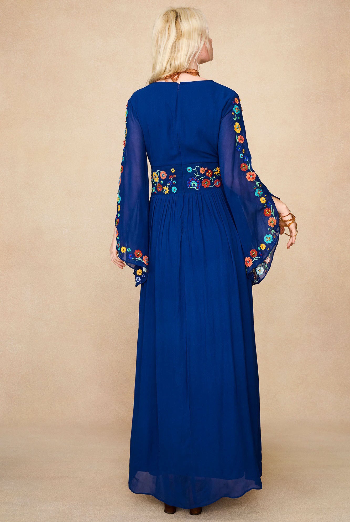 Back view of model in The Hippie Shake's blue vintage embroidered maxi dress showing floral embroidery on waistband and sleeves.