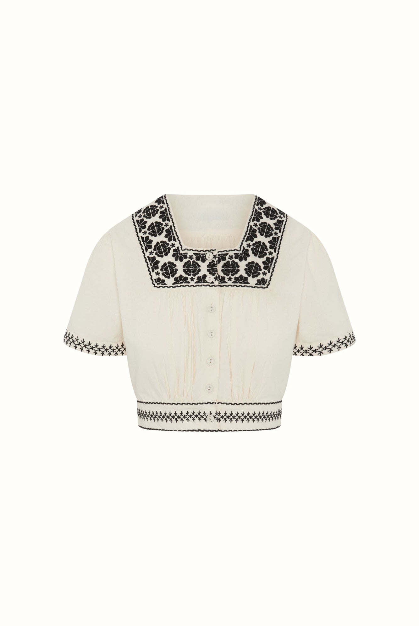 Flat lay of The Hippie Shake's cream embroidered floral crop top with contrast black floral embroidery and buttons.