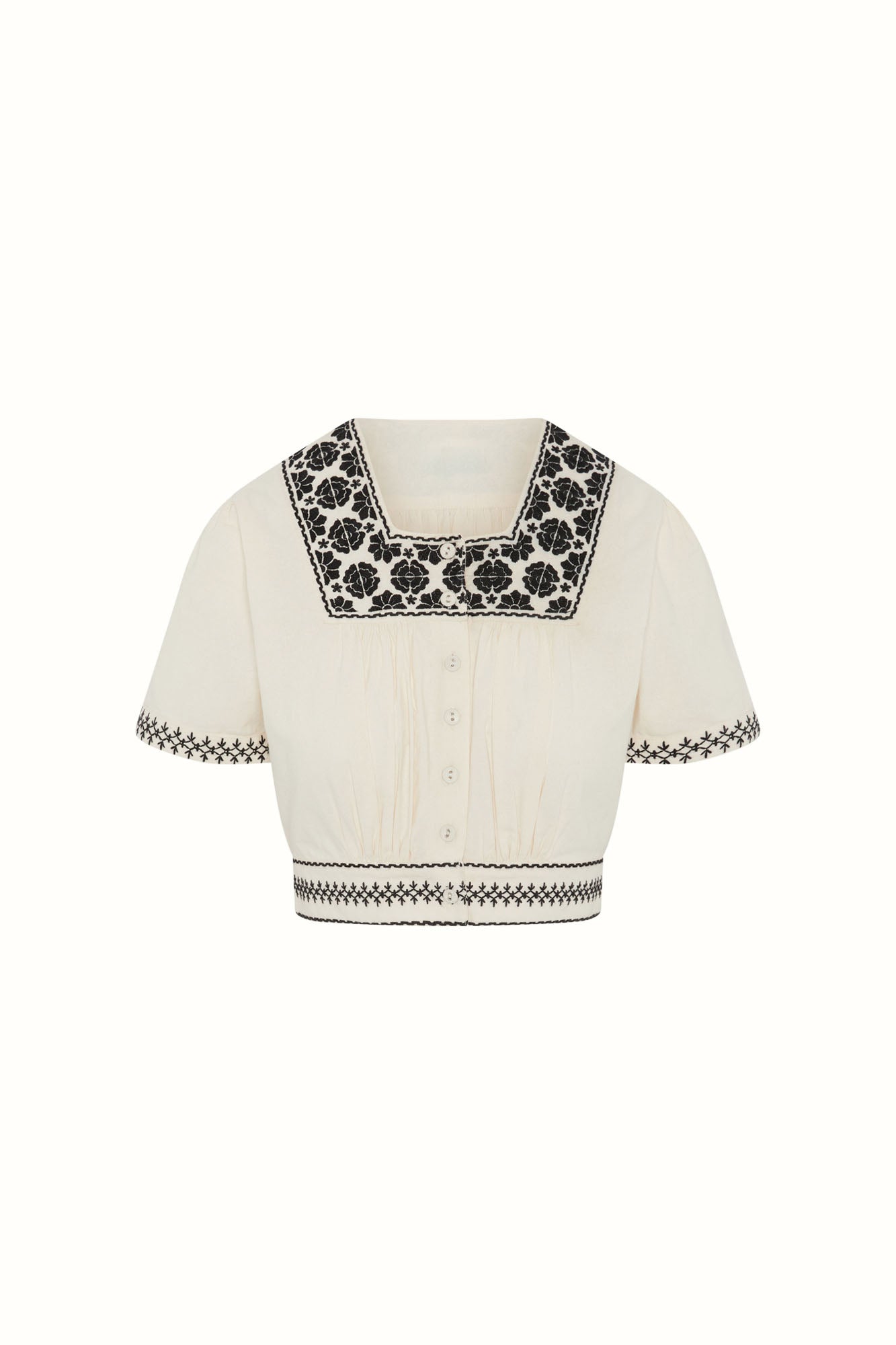 Flat lay of The Hippie Shake's cream embroidered floral crop top with contrast black floral embroidery and buttons.