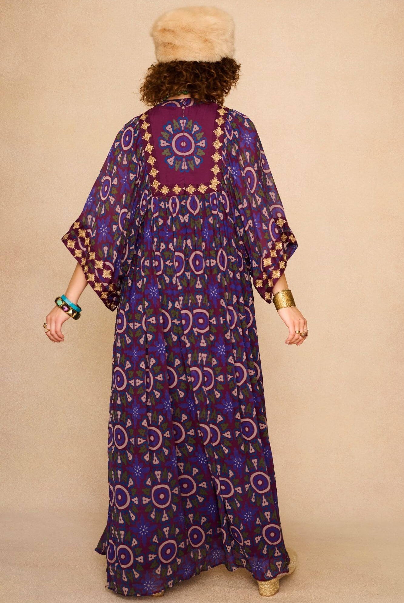 Model wearing a 70s style bohemian maxi dress in a printed purple fabric with hand embroidery - back view