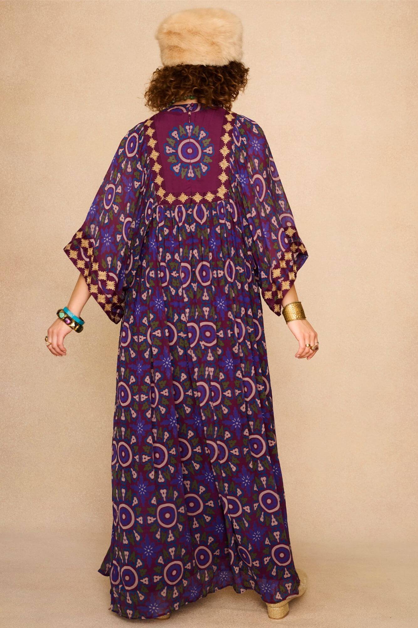 Model wearing a 70s style bohemian maxi dress in a printed purple fabric with hand embroidery - back view
