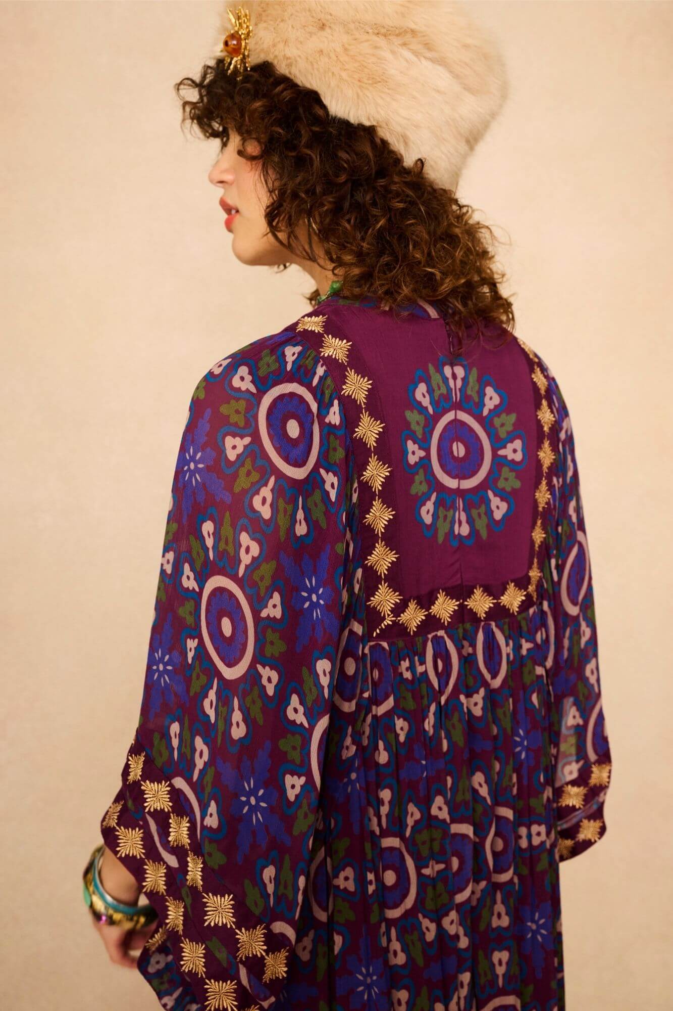 Model wearing a 70s style bohemian maxi dress in a printed purple fabric with hand embroidery - back view close up