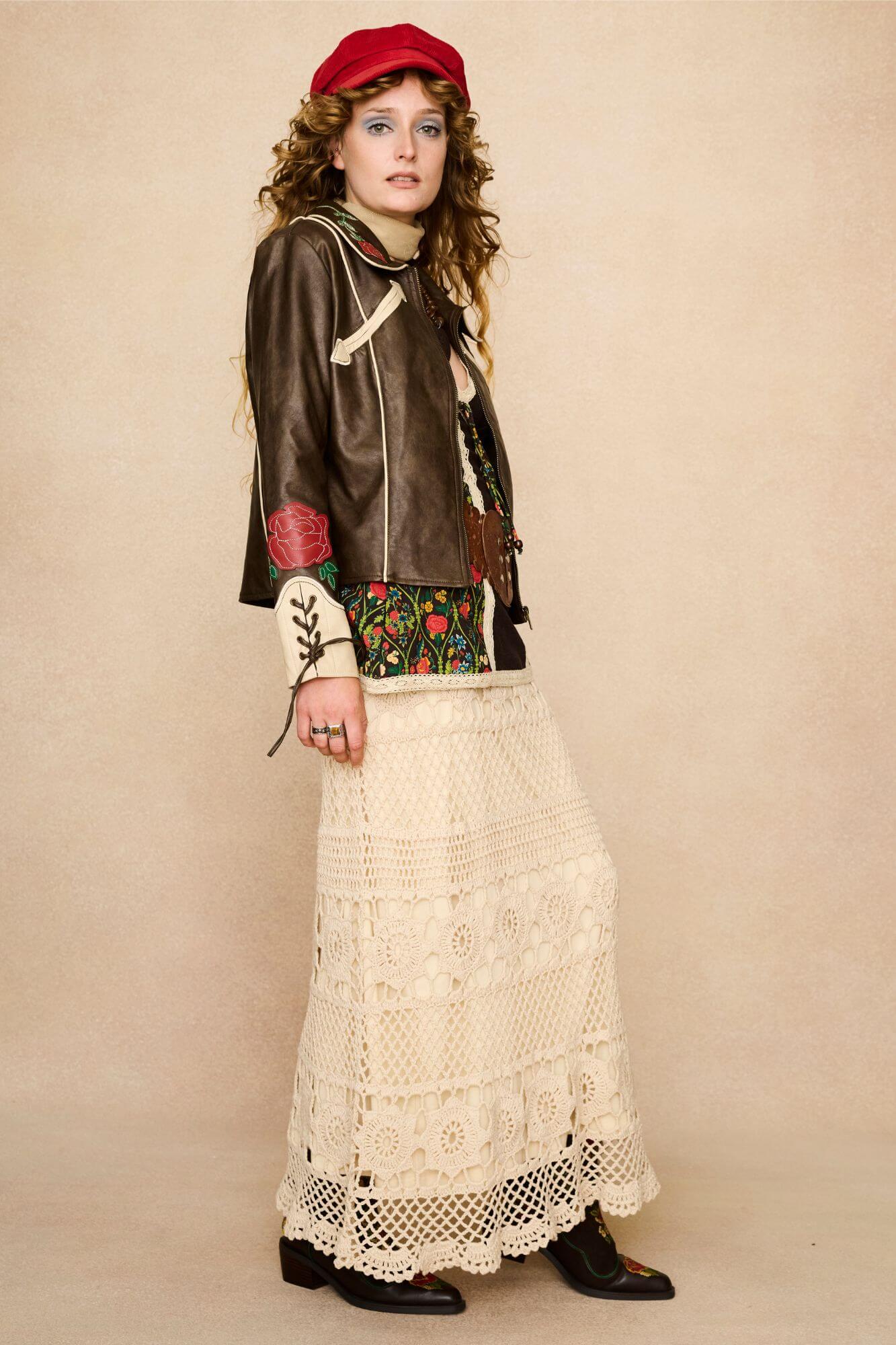 Model wearing a brown 70s style faux leather jacket with red floral embroidery against a beige background - side outfit view