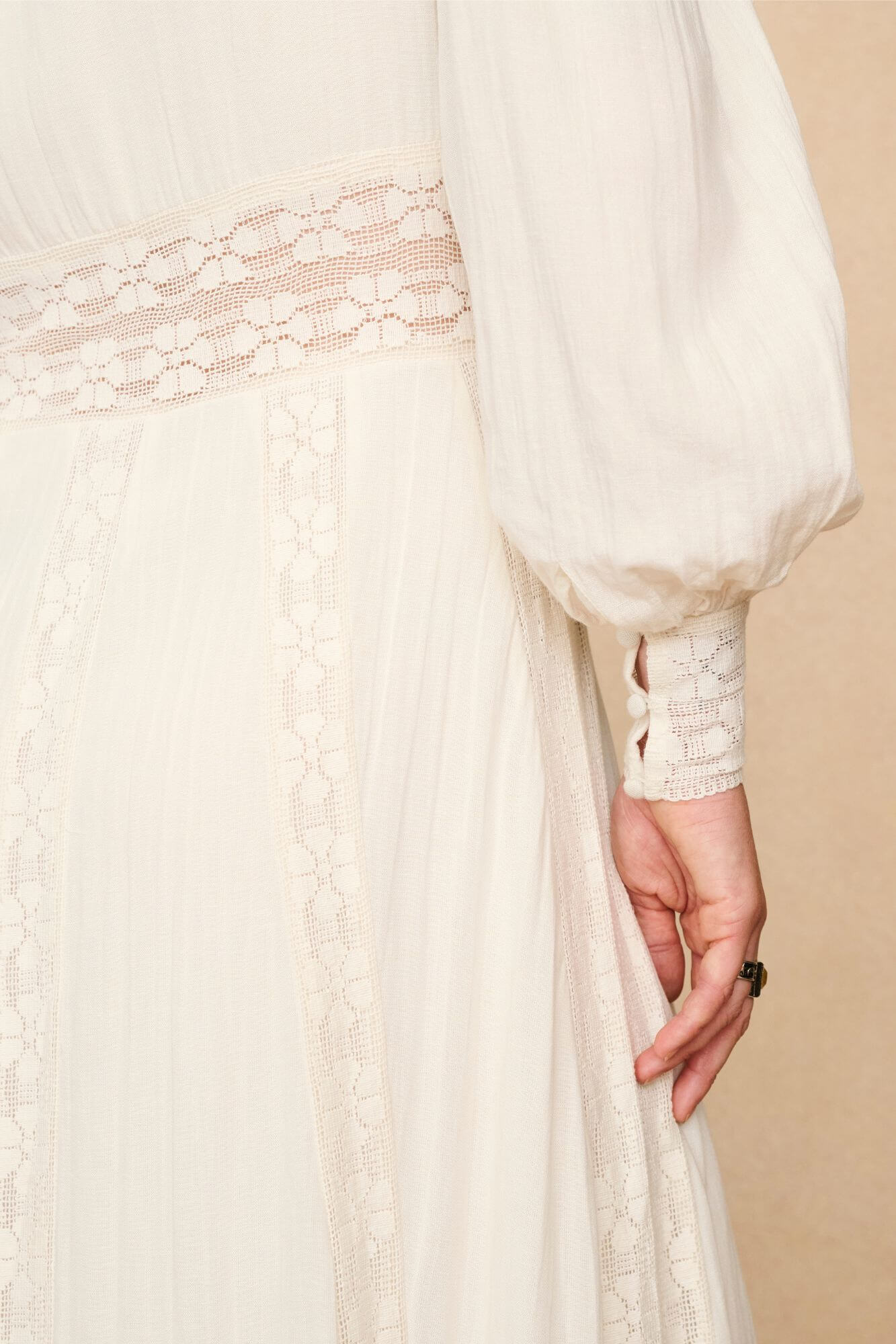Woman in a long cream lace floaty 70s style maxi dress against a beige background - close up sleeve detail