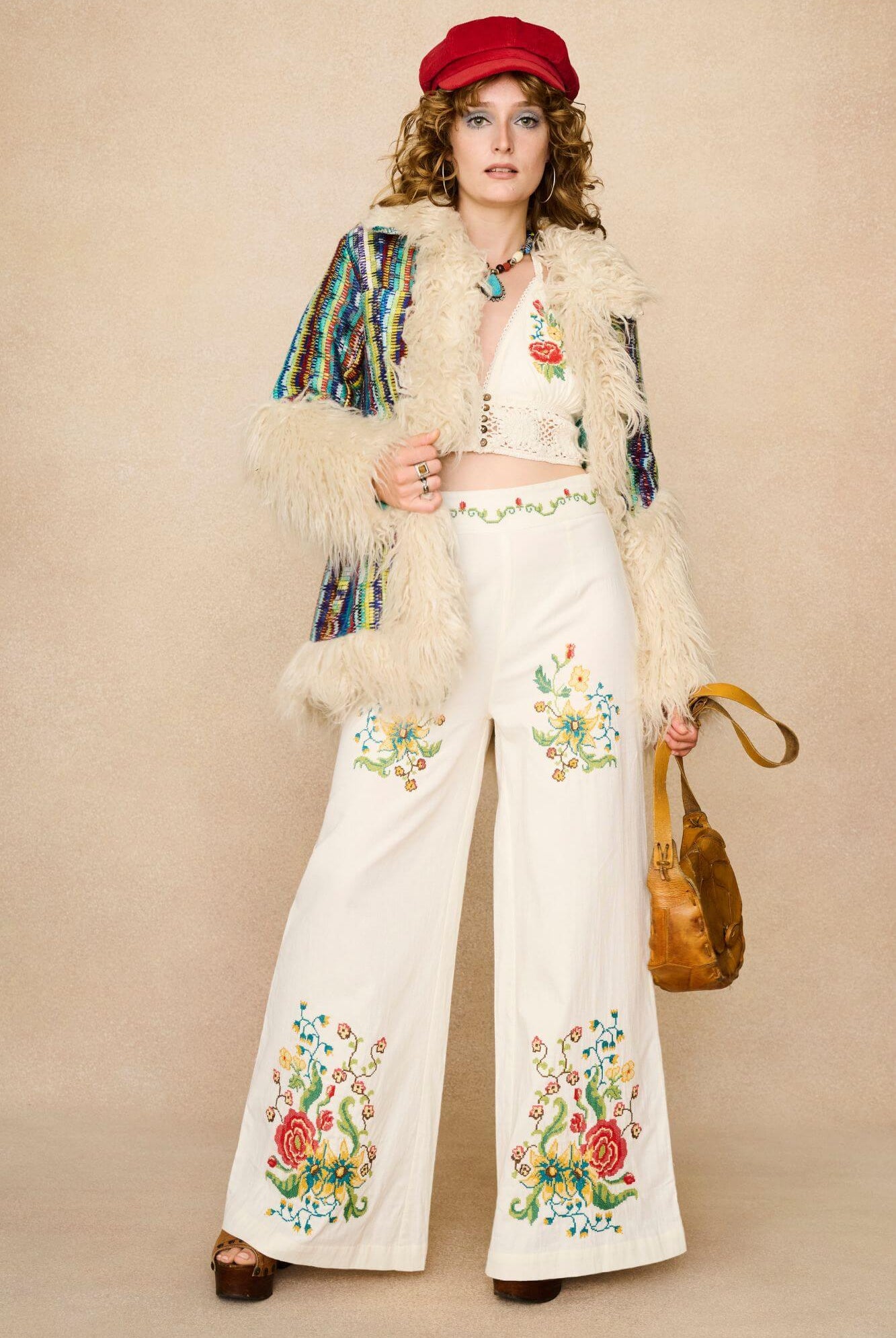 Woman wearing a red cap, floral embroidered top, and colourful necklace against a beige background - outfit combination