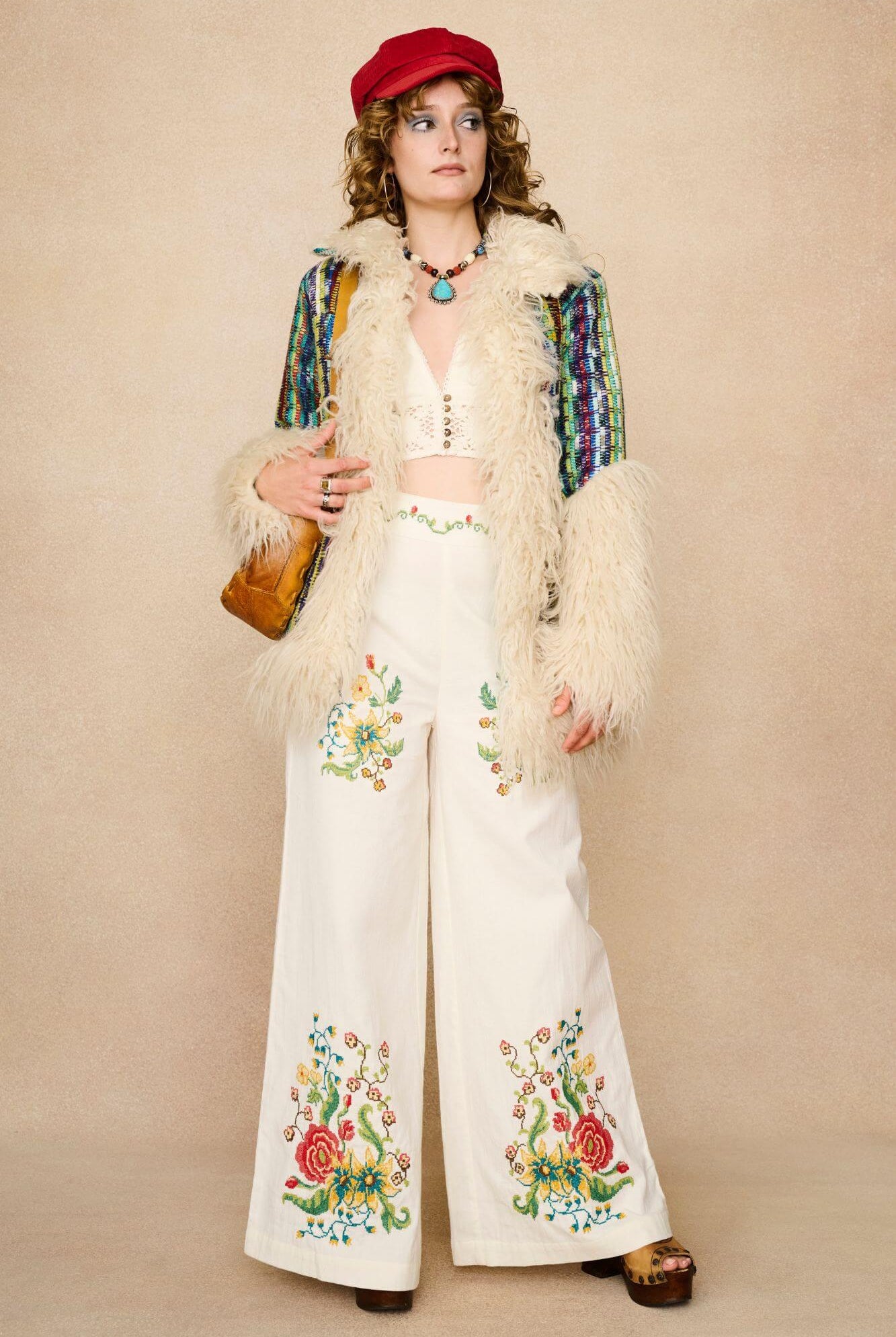 Model wearing white flared trousers with colourful floral embroidery on a beige background - styled outfit suggestion