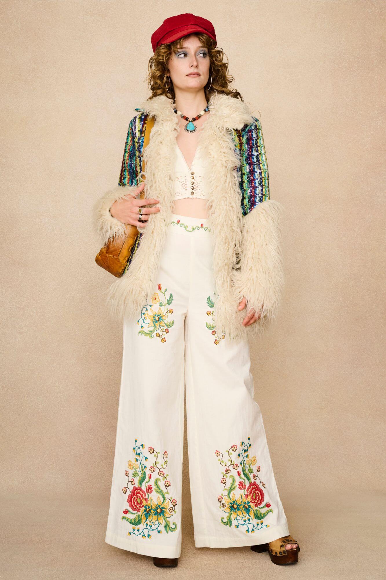 Model wearing white flared trousers with colourful floral embroidery on a beige background - styled outfit suggestion