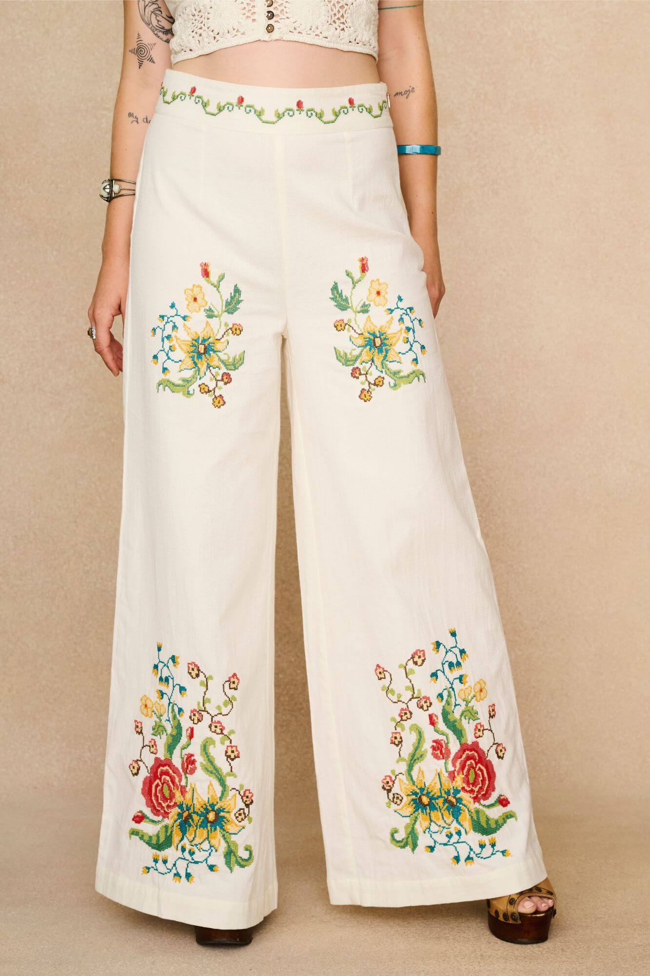 White flared trousers with colourful floral embroidery on a beige background - front view