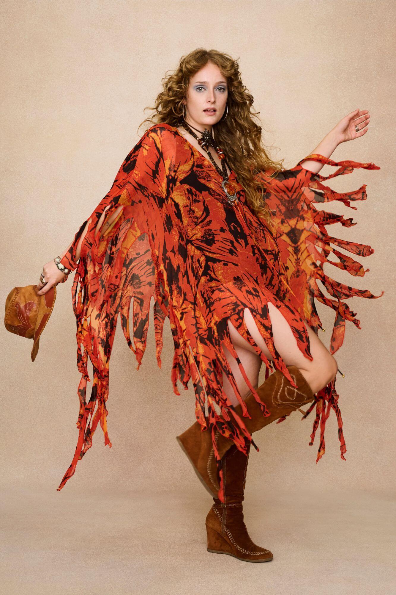 Model wearing a vibrant red and black patterned dress cape with fringe against a beige background - With movement