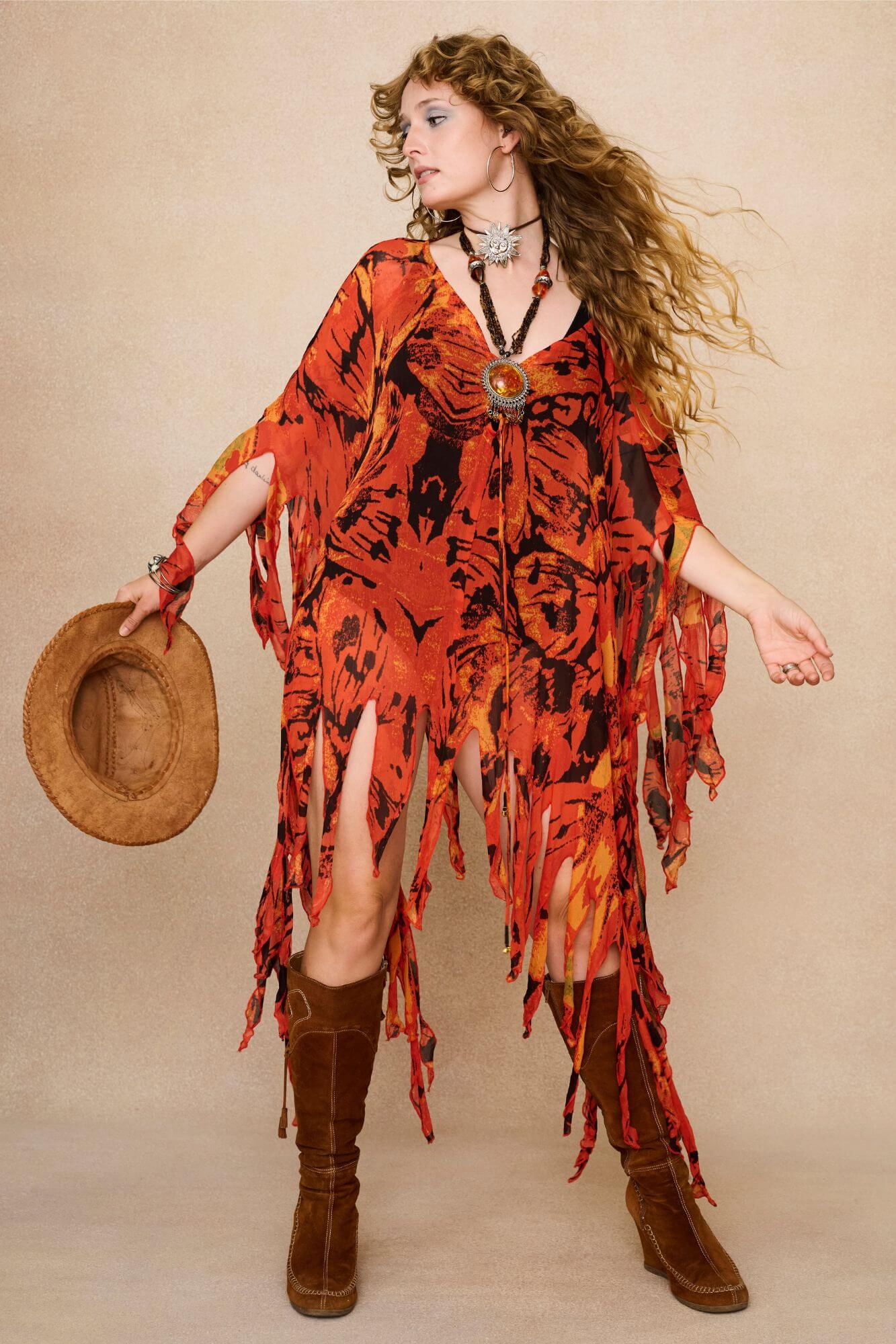 Model wearing a vibrant red and black patterned dress cape with fringe against a beige background - Front view