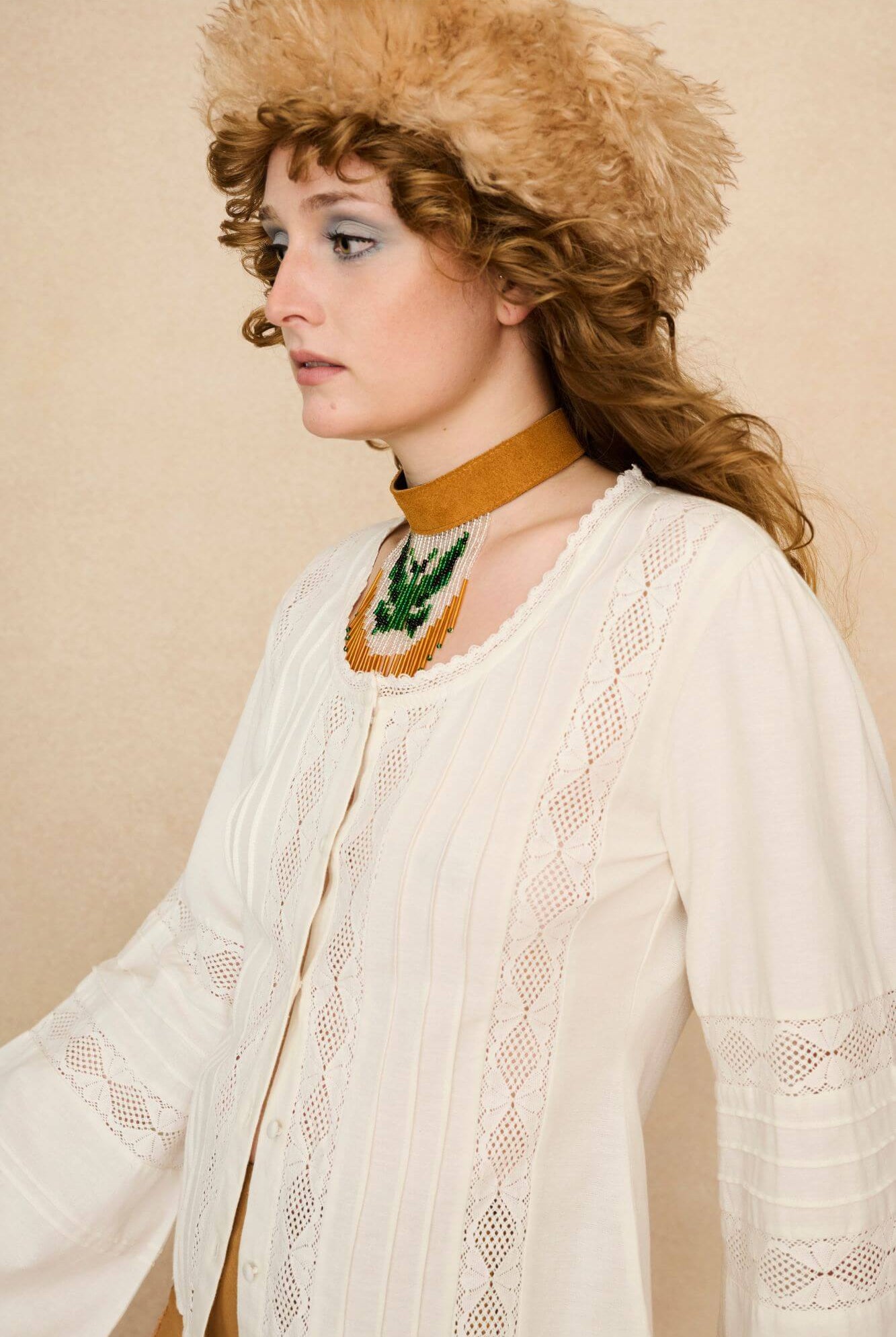 Woman wearing a white lace blouse and 70s style pants against a beige background - detail close up