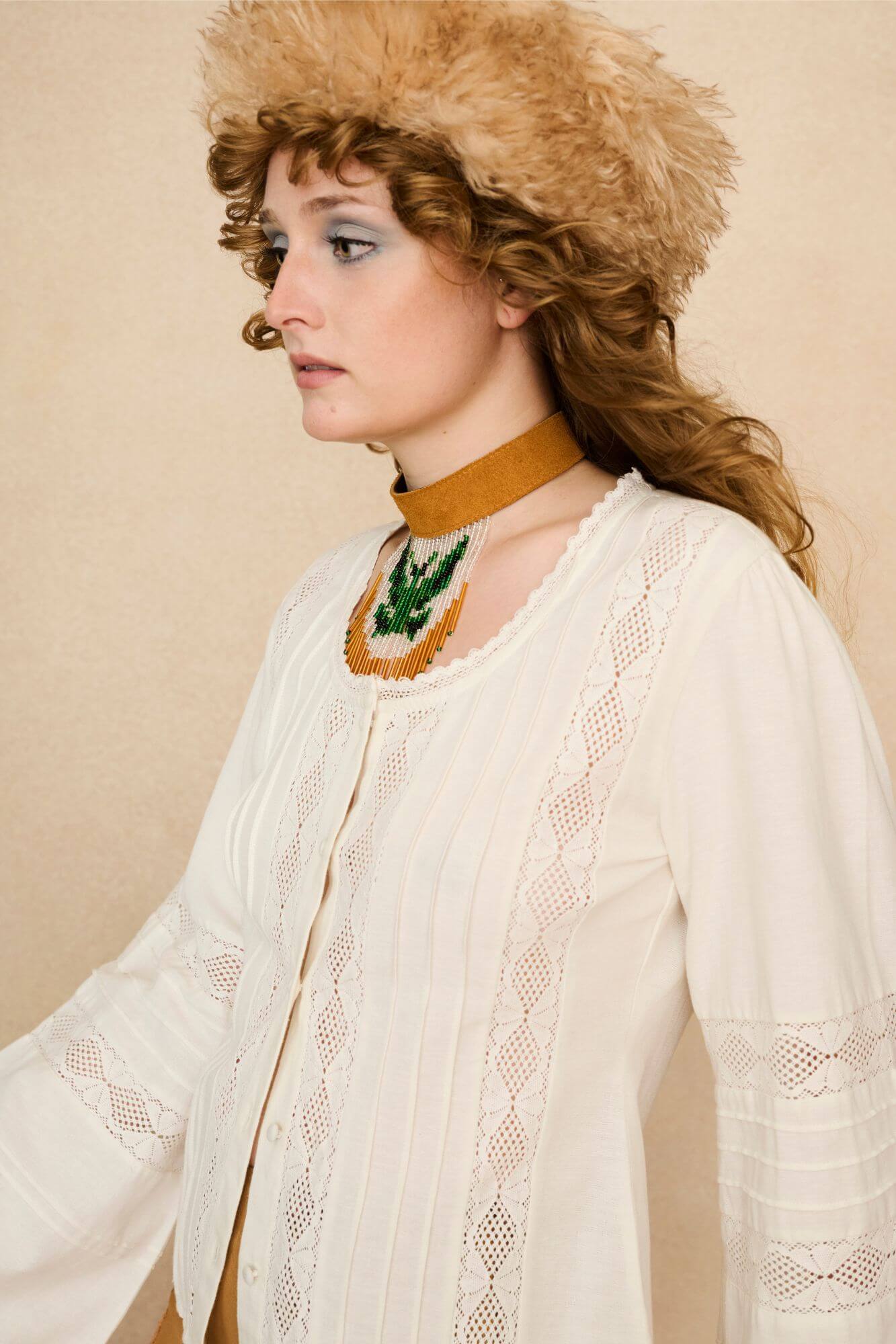 Woman wearing a white lace blouse and 70s style pants against a beige background - detail close up