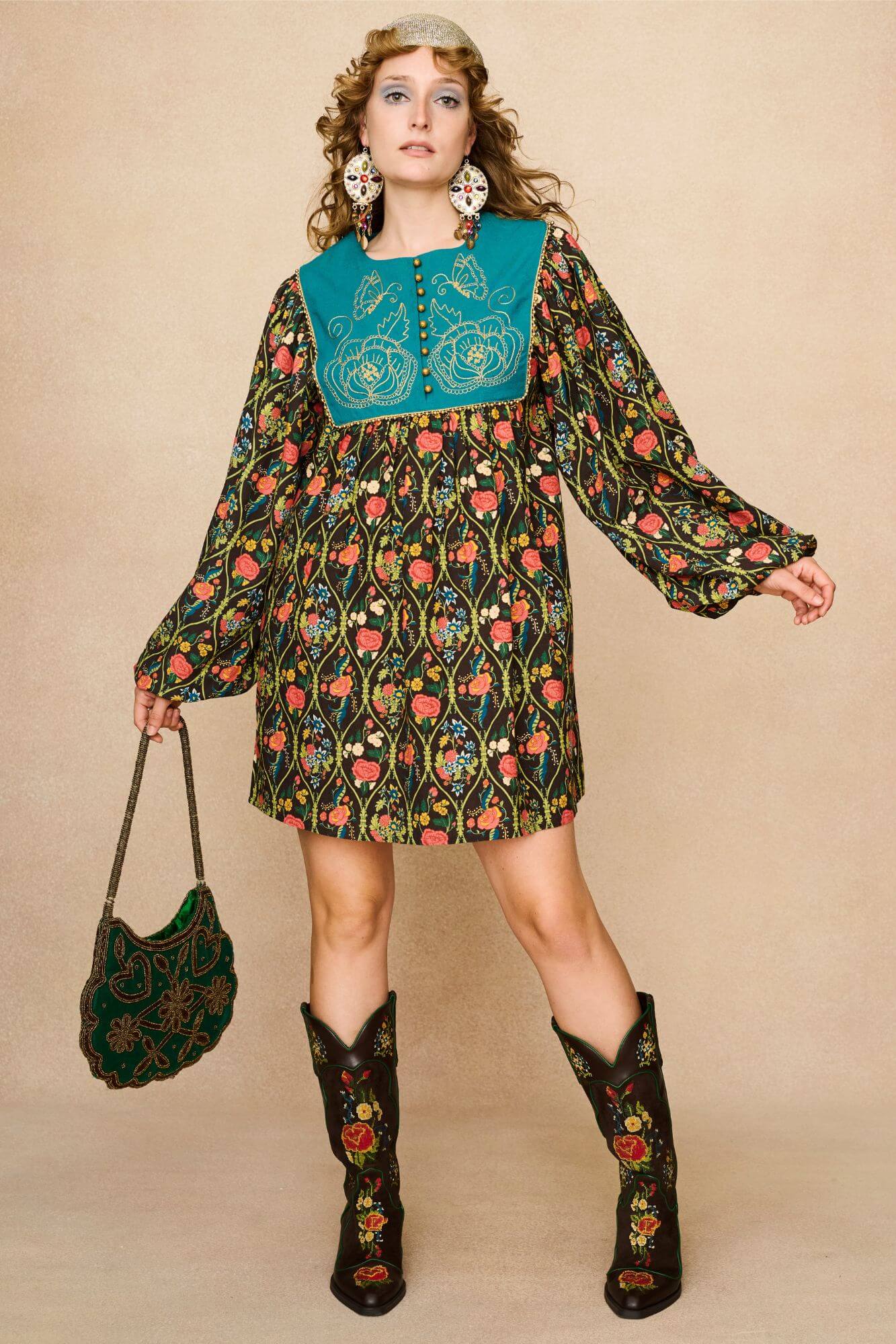 Model wearing a 70s style floral mini dress and matching boots against a beige background - front view